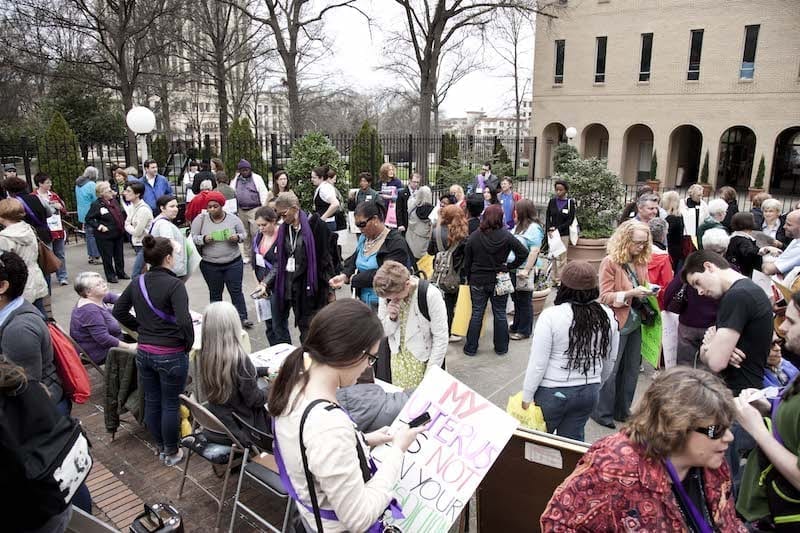 Demonstrators holding signs and talking at an outdoor rally.