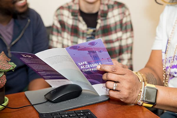 A close-up image of a staff member walking patients through a pamphlet entitled “Safe, Accessible, Compassionate”