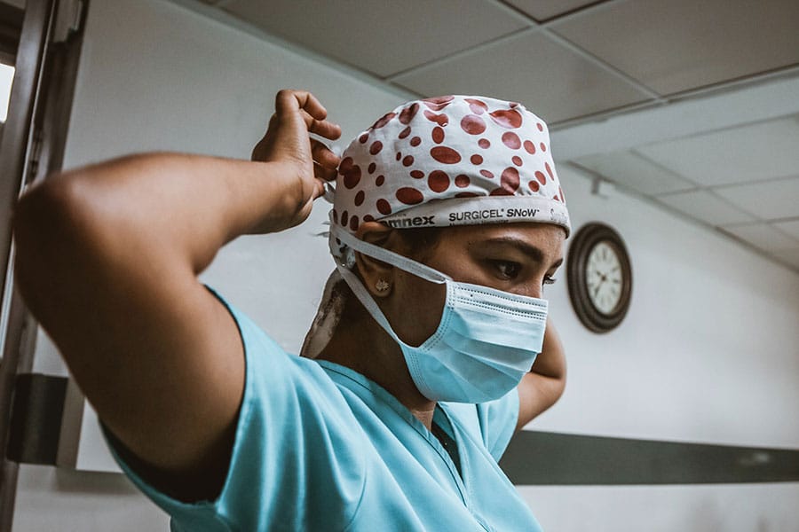 Model posing as staff member wearing scrubs, mask, and cap.