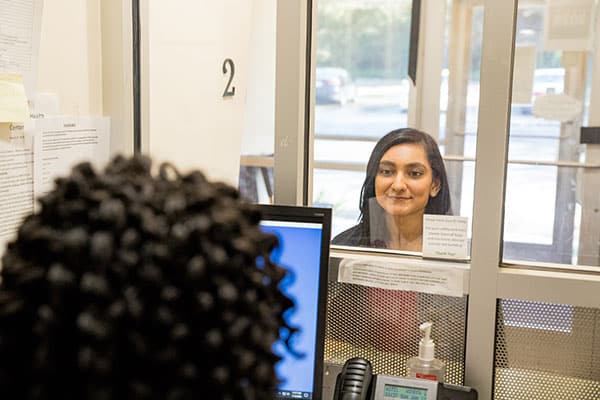 A model poses as a patient speaking with a staff member at the front desk.
