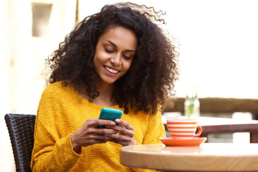 Model looking at phone while seated at table with mug.