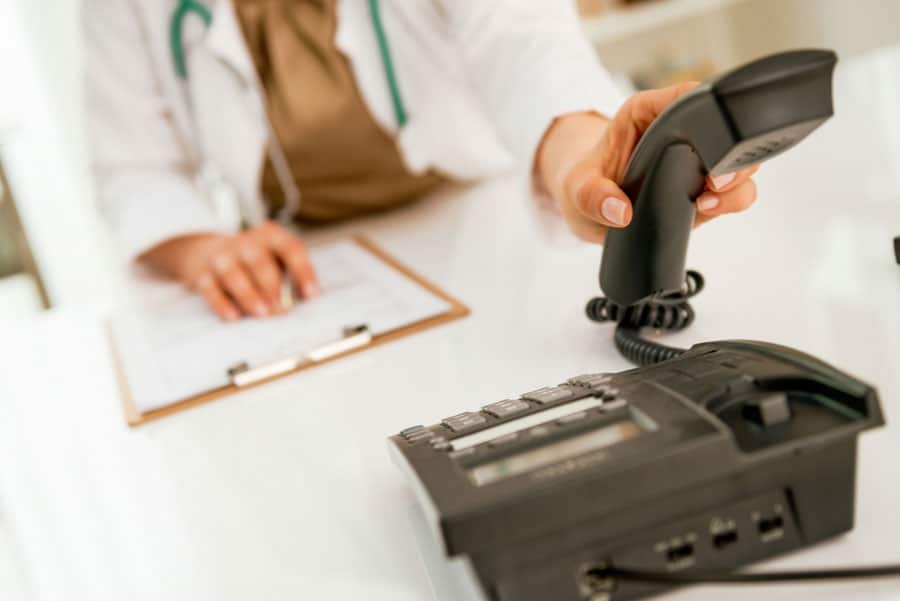Office staff member in white coat answering phone.