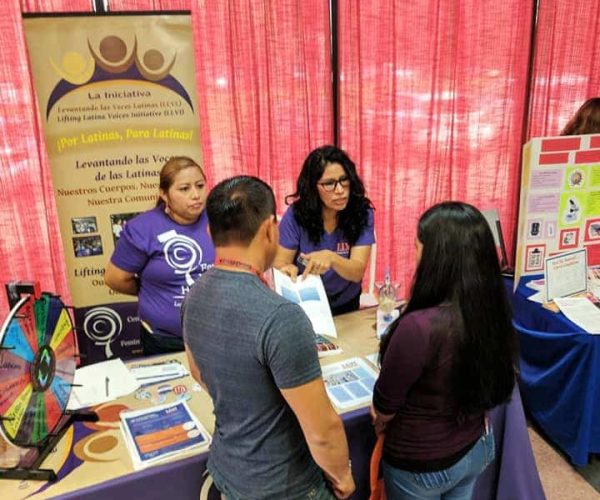 Two Lifting Latinx Voices Initiative members share information with event attendees at their table.