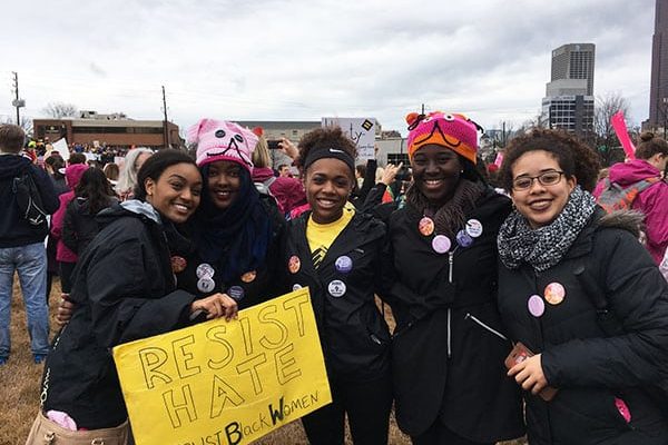 Four smiling demonstrators holding a sign that reads “Resist Hate. Trust Black Women.”