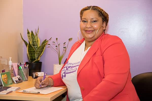 A clinic staffer smiles at the camera while sitting at a desk.